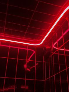 a bathroom with red neon lights on the ceiling and tiled walls, along with a shower head