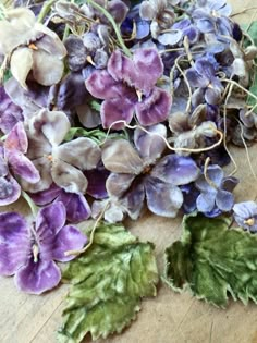 purple and green flowers are laying on a wooden table next to each other, with leaves scattered around them