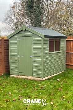 a green shed sitting in the middle of a lush green yard next to a wooden fence