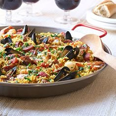 a pan filled with rice and mussels on top of a table next to wine glasses