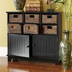 a black cabinet with wicker baskets on top and two vases next to it