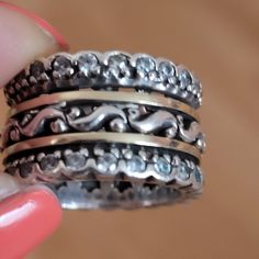 a stack of silver rings sitting on top of a wooden table next to a pink manicure