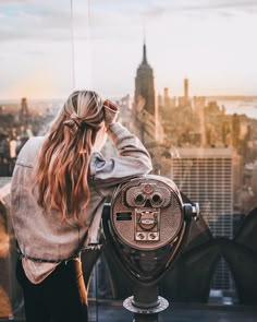 a woman looking at the city from top of a building with a telescope in her hand