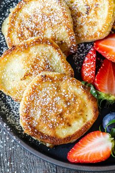 french toast with powdered sugar and strawberries on a black plate, ready to be eaten