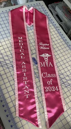 a pink ribbon that says medical assistant class of 2024 on it, sitting on top of a cutting mat