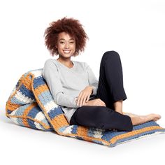 a woman is sitting on a multicolored knitted blanket and smiling at the camera