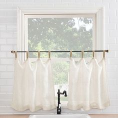 a kitchen sink under a window with white curtains hanging from it's side and a black faucet