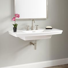 a white bathroom sink sitting under a mirror next to a wall mounted faucet