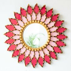 a pink and gold mirror mounted to the side of a white wall next to a plant