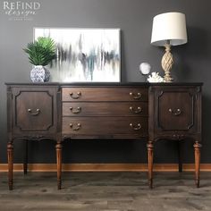 an antique dresser with three drawers and two lamps on top, against a gray wall