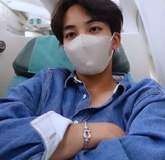 a young man wearing a face mask sitting in a chair with his arms crossed and looking at the camera