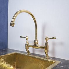 a gold sink with two faucets on the side and a blue wall behind it