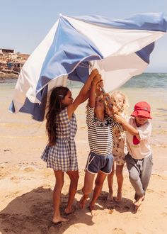 three children are playing with an umbrella on the beach