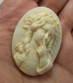 a hand holding a white carved piece of art with a woman's face on it