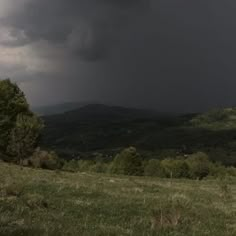 a storm rolls in over the mountains on a cloudy day with trees and grass below