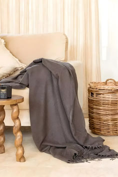 a couch with a blanket on top of it next to a table and wicker basket