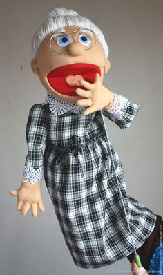 an old woman puppet is holding a red object in her hand and looking at the camera