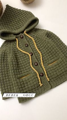 a green knitted sweater with buttons and hood on it, next to some nuts