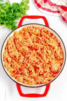 a red pot filled with rice and garnished with parsley on the side