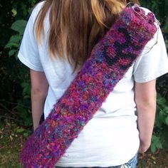 a woman with long brown hair wearing a purple knitted neckwarf in front of some bushes