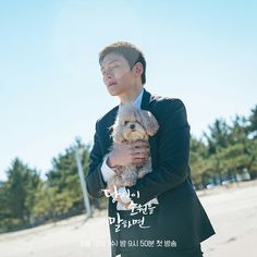 a man in a suit holding a small dog while standing on top of a beach