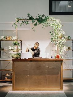 a person sitting at a desk with plants on it and shelves in the back ground