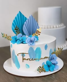 there is a white cake with blue flowers on the top and gold leaves on the bottom