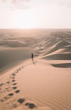 a person standing in the middle of a desert with footprints on the ground and sand dunes