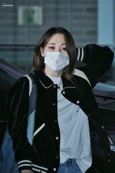 a woman wearing a face mask while standing in front of a car with her hand on her head