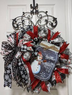 a christmas wreath hanging on a door with snowman and red ribbon around the front