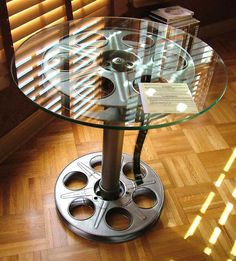 a round glass table with metal wheels on the top and bottom, in front of a wooden floor