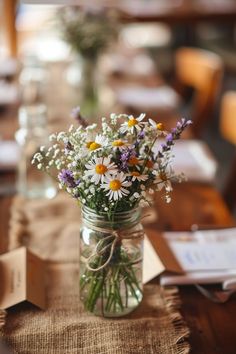 a mason jar filled with wildflowers sitting on top of a table covered in burlap