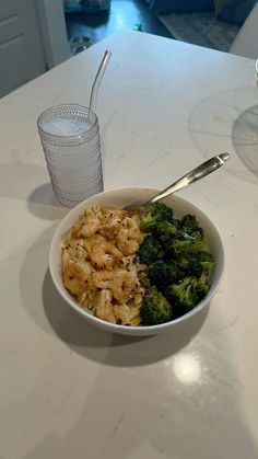 a bowl of food with broccoli and rice next to a glass of water