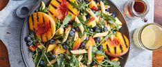 a salad with peaches, blueberries and spinach on a plate next to a glass of orange juice