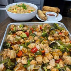 a pan filled with chicken and vegetables next to a bowl of rice