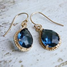 two pairs of earrings with blue stones hanging from gold earwires on a marble surface