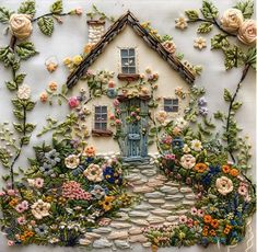 a house made out of flowers and plants on a white surface with a blue door