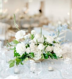 white flowers and greenery are arranged on a table with silverware, glasses and candles