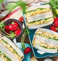 four sandwiches with tomatoes and lettuce in them on blue trays next to eggs