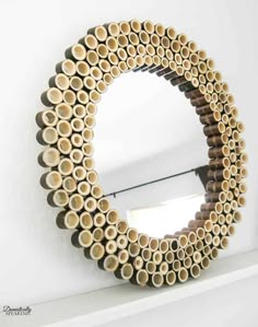 a circular mirror made out of wooden logs on top of a white shelf next to a window