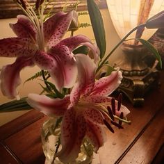 a vase filled with pink flowers sitting on top of a wooden table next to a lamp