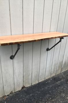 a wooden shelf sitting on top of a wall next to a metal pipe and hook