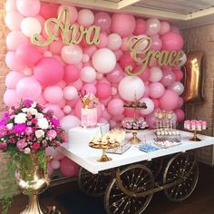 a table topped with lots of pink and white balloons next to a wall covered in gold letters