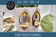 a pair of earrings with the words baby jesus earings printed on them, sitting next to a potted plant