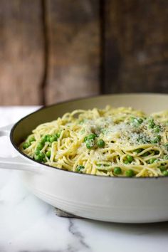 pasta with peas and parmesan cheese in a skillet on a marble table