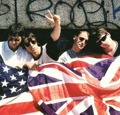 three young men holding an american flag in front of graffiti