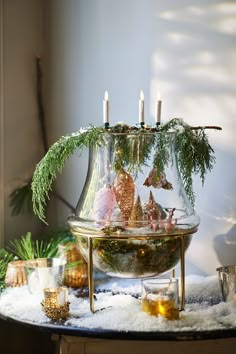 a glass vase filled with candles on top of a table covered in snow and pine branches