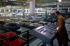 a man standing next to a machine in a factory filled with old cars and trucks