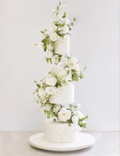 a three tiered wedding cake with white flowers on top and greenery in the middle