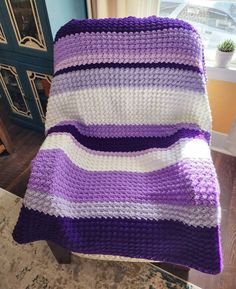 a purple and white crocheted blanket sitting on top of a chair